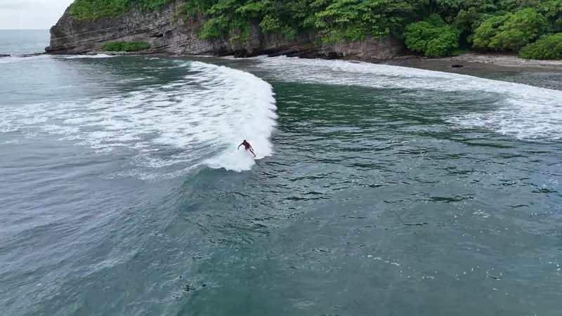 A surfer riding a wave, seen from a drone
